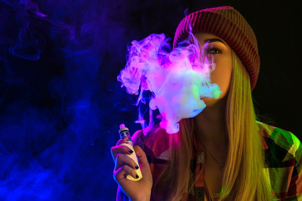 Young woman with long hair vaping whilst looking at camera